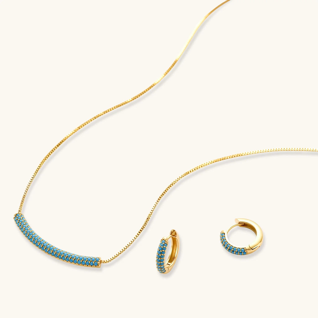 Gold-plated curved necklace and hoop earrings with turquoise cubic zirconia stones on white background.
