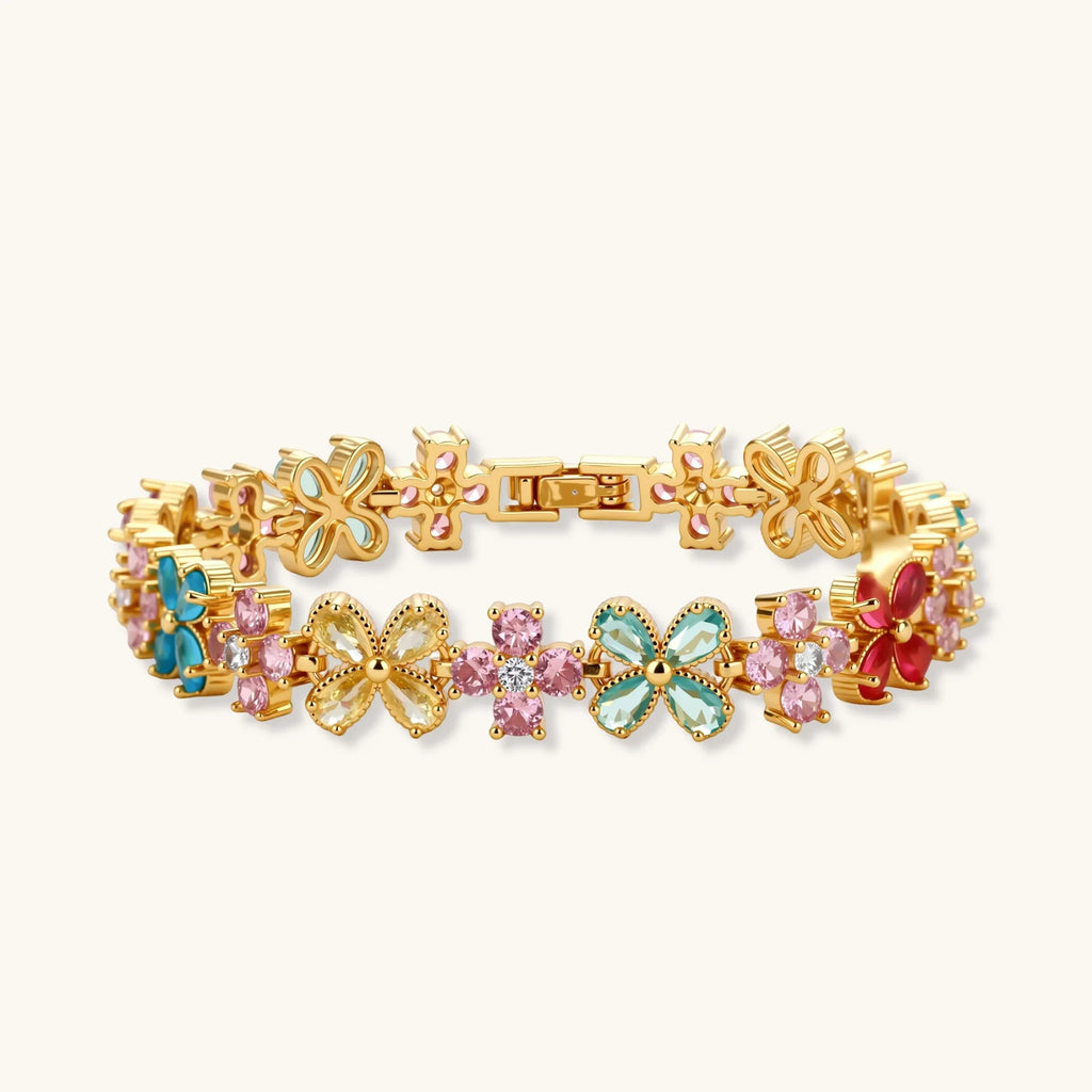 Gold-plated flower necklace, bracelet and drop earrings with multicolor zirconia petals and white round beads on a cream background.