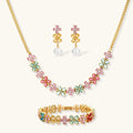 Gold-plated flower necklace, bracelet and drop earrings with multicolor zirconia petals and white round beads on a cream background.