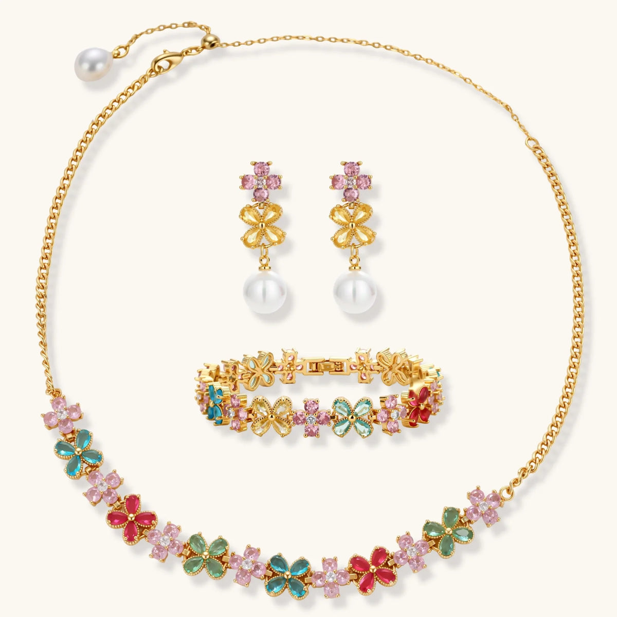 Gold-plated flower necklace, bracelet and drop earrings with multicolor zirconia petals and white round beads on a cream background.