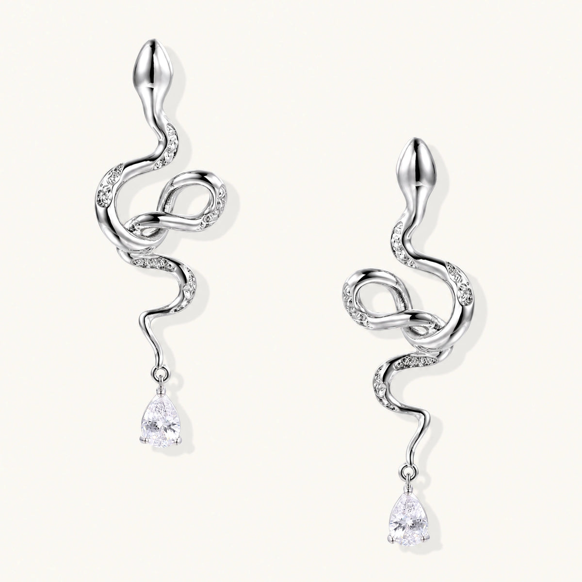 Silver snake-shaped drop earrings with crystal accents and teardrop stone dangles on cream background.