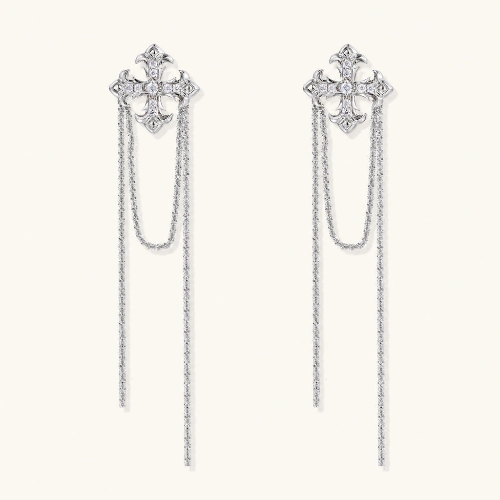 White gold plated baroque cross stud earrings with long cascading zirconia chains on cream background