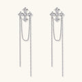 White gold plated baroque cross stud earrings with long cascading zirconia chains on cream background