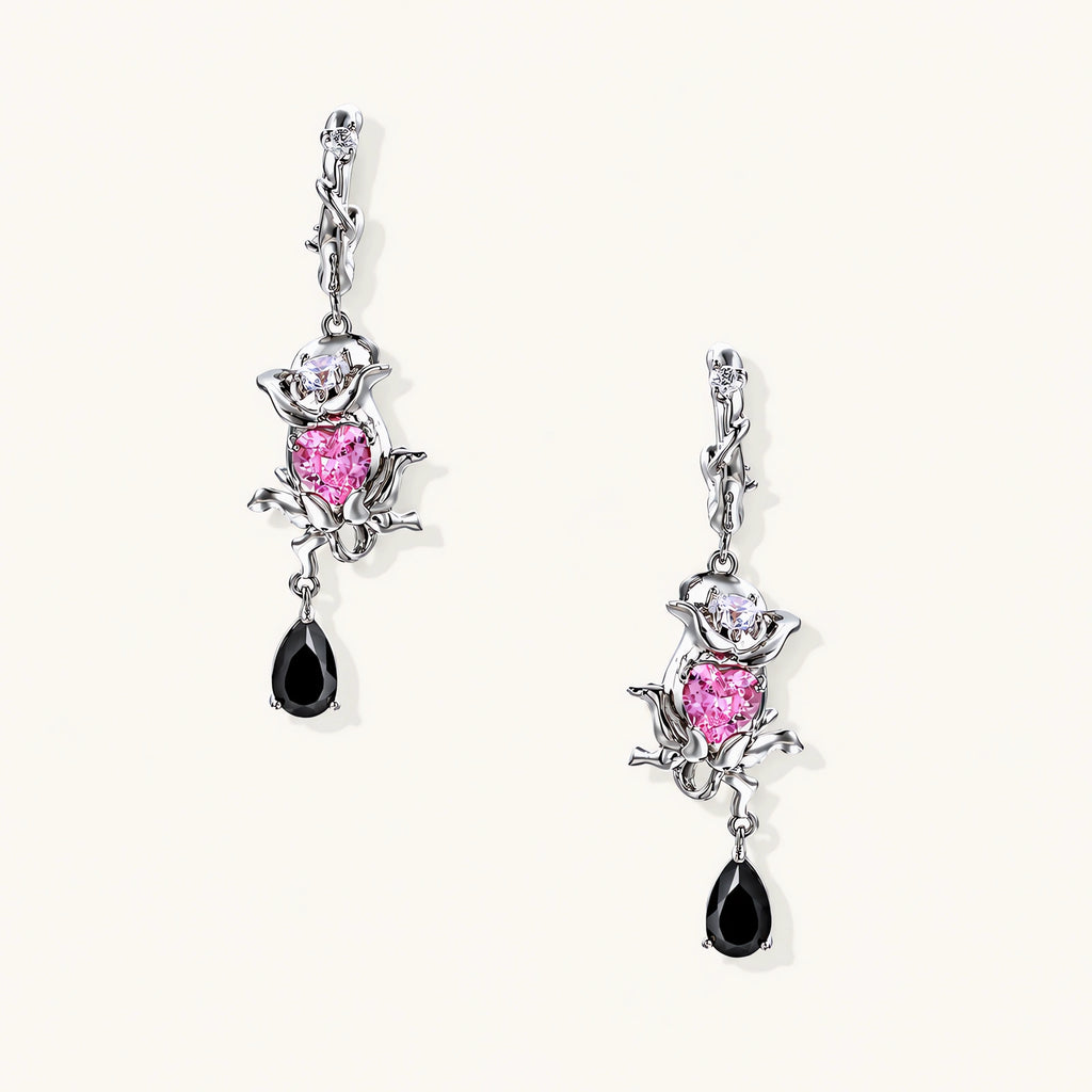 Silver-toned drop earrings with ornate rose design, pink zirconia center, and black teardrop stones on cream background