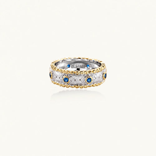 Two-tone ring with brushed silver center, gold beaded edges, and blue zirconia stones on white background.