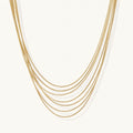 Seven delicate gold-plated snake chains create an elegant layered necklace on a neutral background.