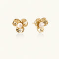Gold-plated flower stud earrings with textured petals and centered freshwater pearl on beige background