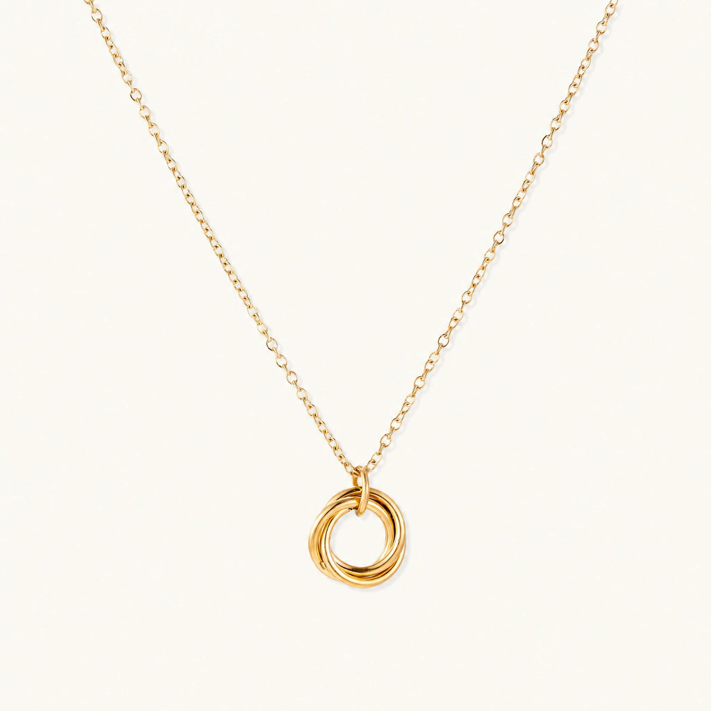 Delicate gold-plated necklace with three interlocking circle rings forming a minimalist knot pendant on cream background