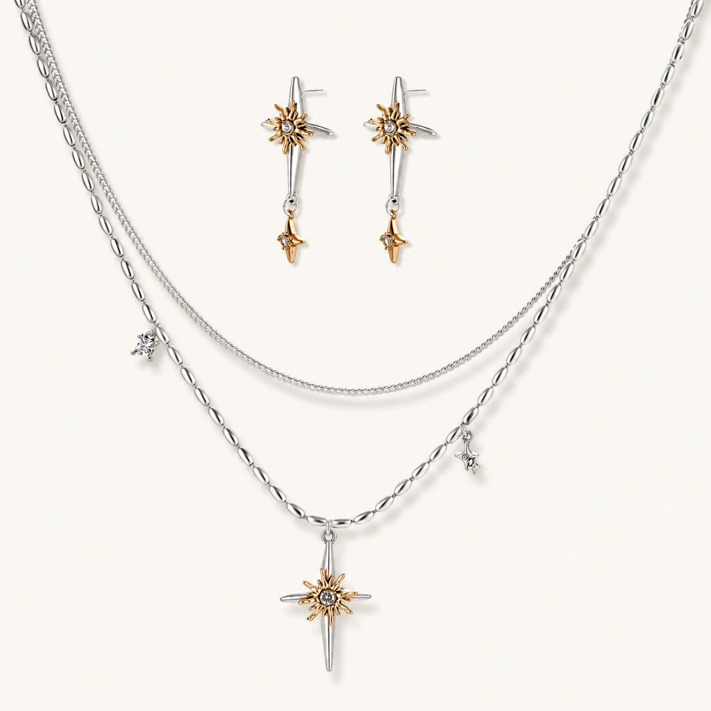 Layered silver-toned necklace set with cross pendant and gold sun charm detail, matching drop earrings on white background.
