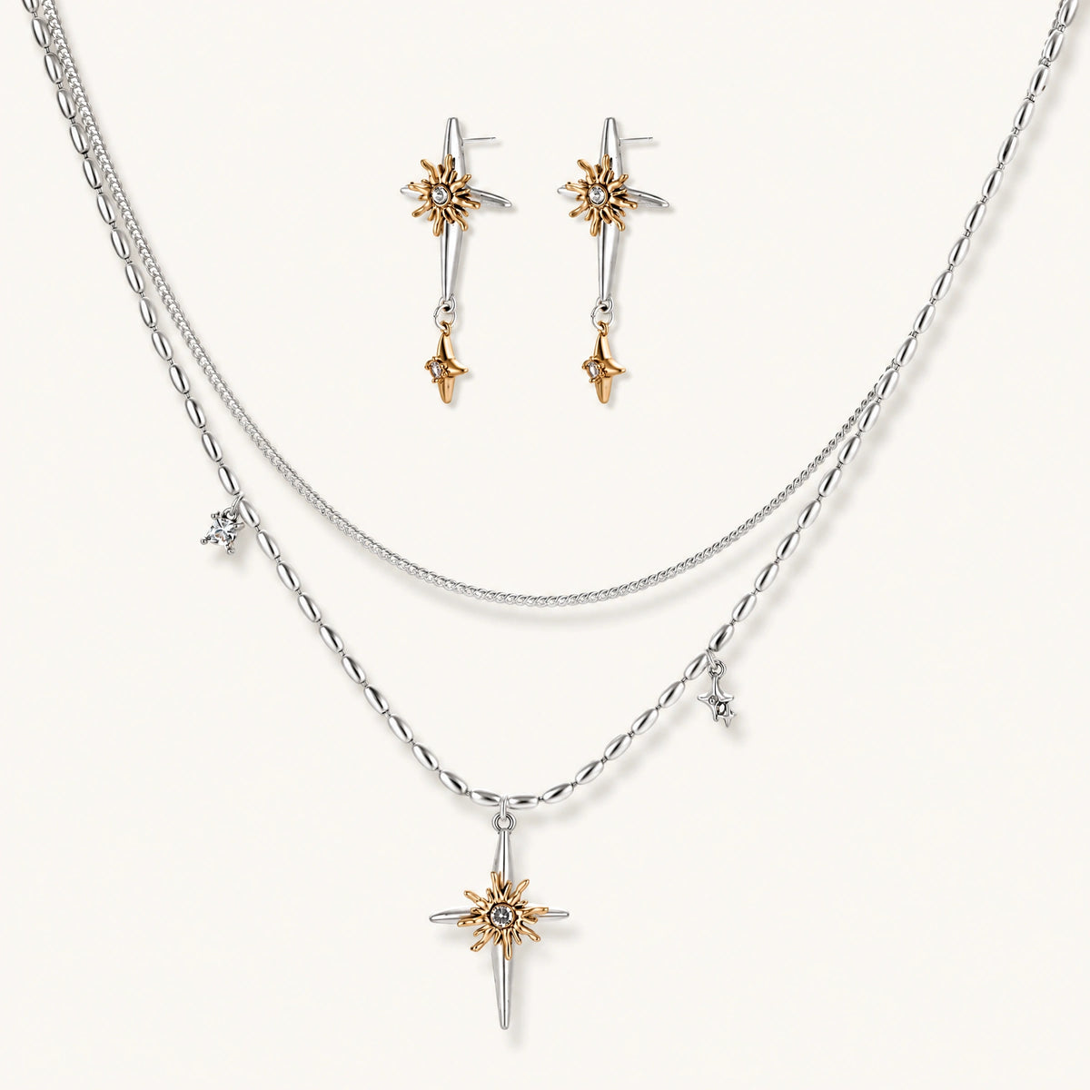 Layered silver-toned necklace set with cross pendant and gold sun charm detail, matching drop earrings on white background.