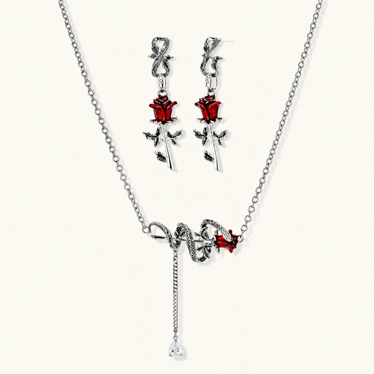 Gothic jewelry set with silver snake designs holding red enamel roses, featuring detailed leaf stems on cream background
