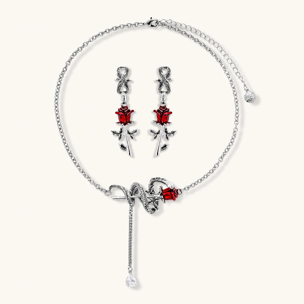 Gothic jewelry set with silver snake designs holding red enamel roses, featuring detailed leaf stems on cream background