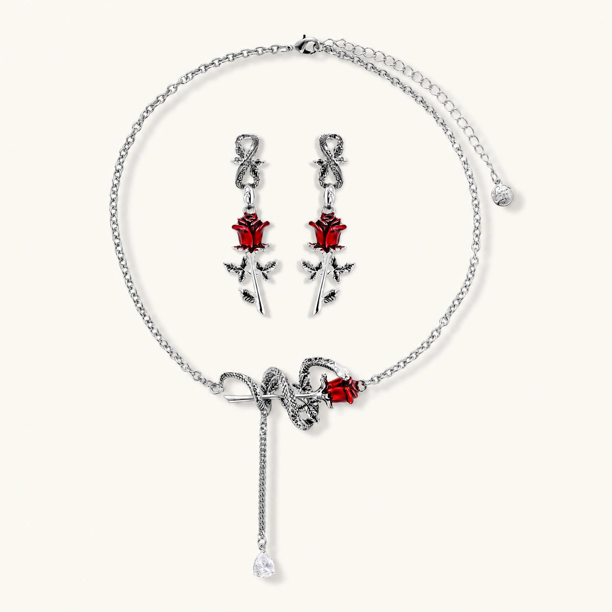Gothic jewelry set with silver snake designs holding red enamel roses, featuring detailed leaf stems on cream background