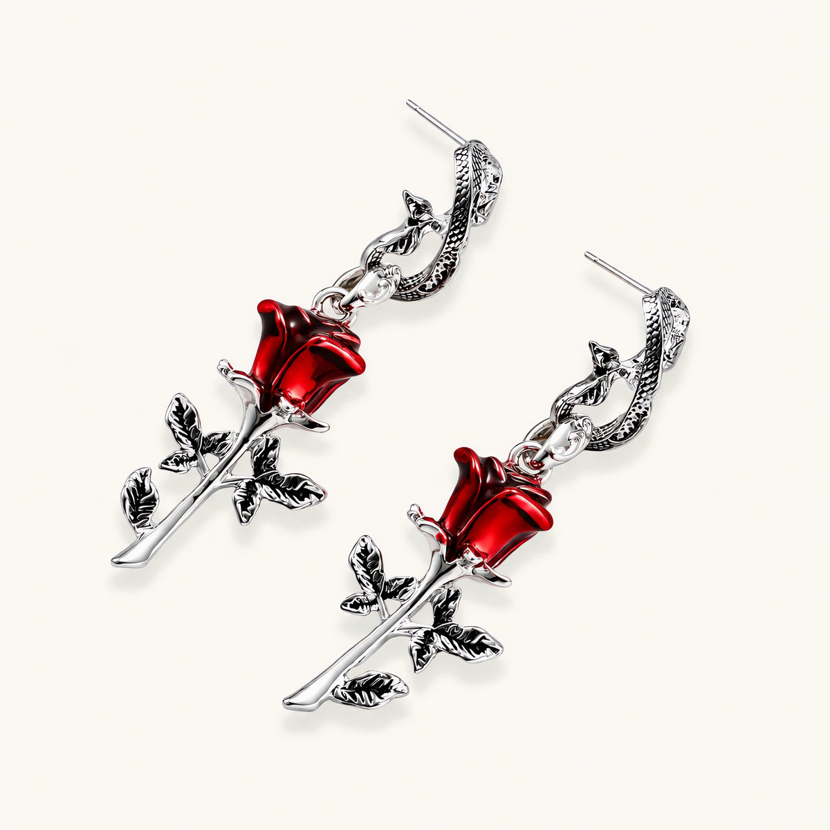 Gothic jewelry set with silver snake designs holding red enamel roses, featuring detailed leaf stems on cream background