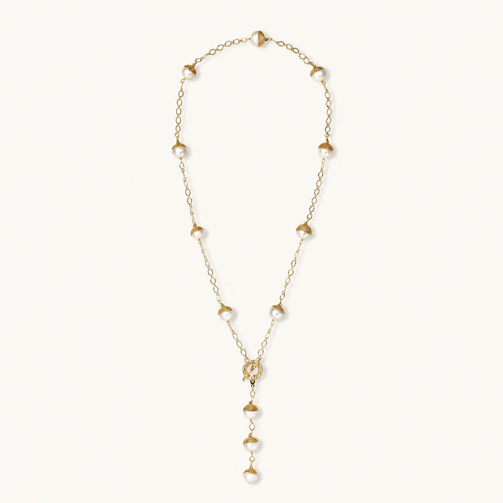 Gold-plated lariat necklace with baroque pearls and textured caps on cream background, showing adjustable Y-shaped design.