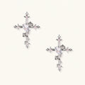 Pair of ornate silver cross earrings with heart-cut clear zirconia center, rose motifs, and spike tips on cream background.
