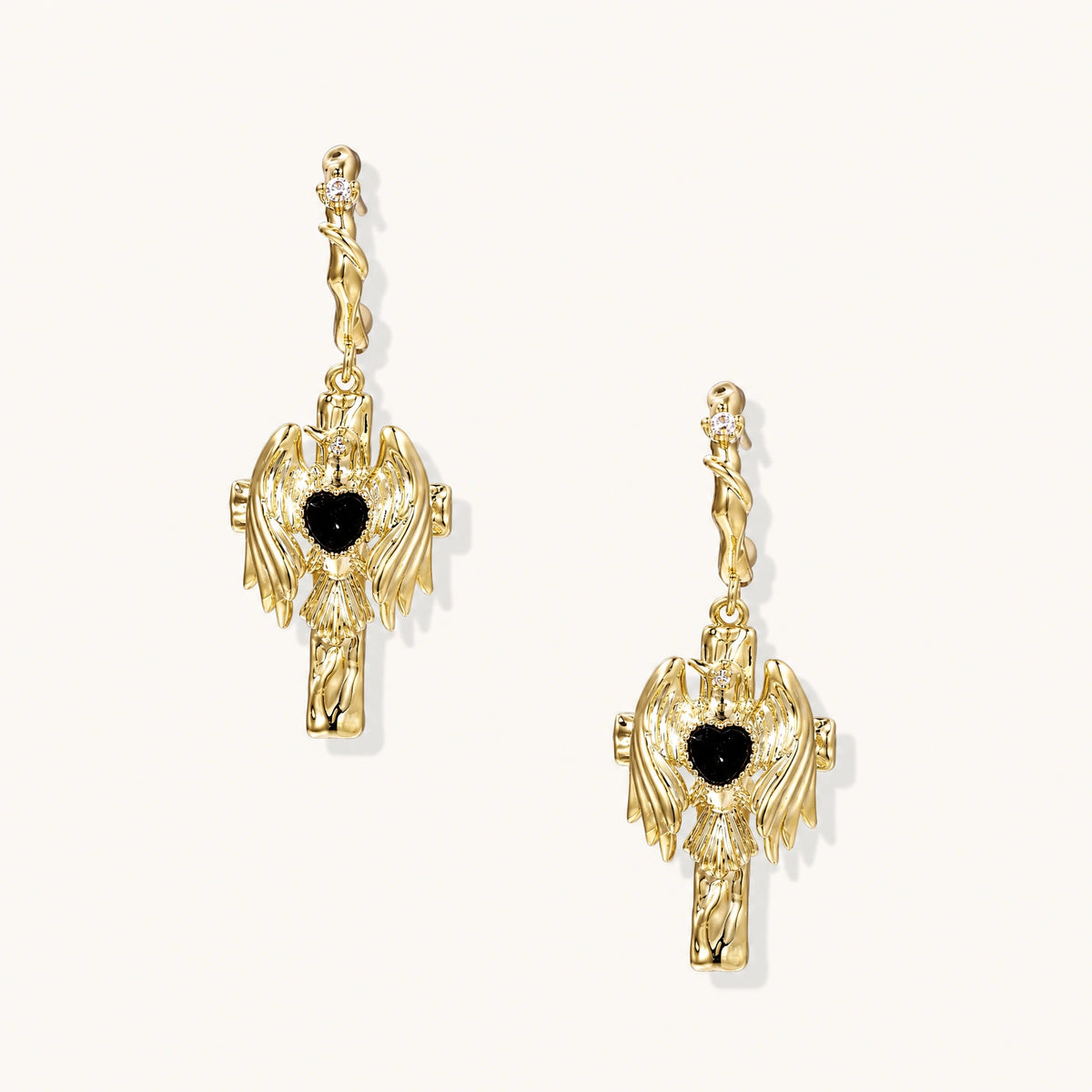 Gold angel wing drop earrings with black heart-shaped zirconia center and twisted posts on beige background