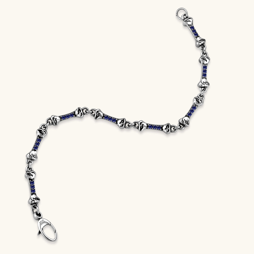 Sterling silver bone-link bracelet with blue cubic zirconia stones and engraved motifs, lobster clasp, on cream background.