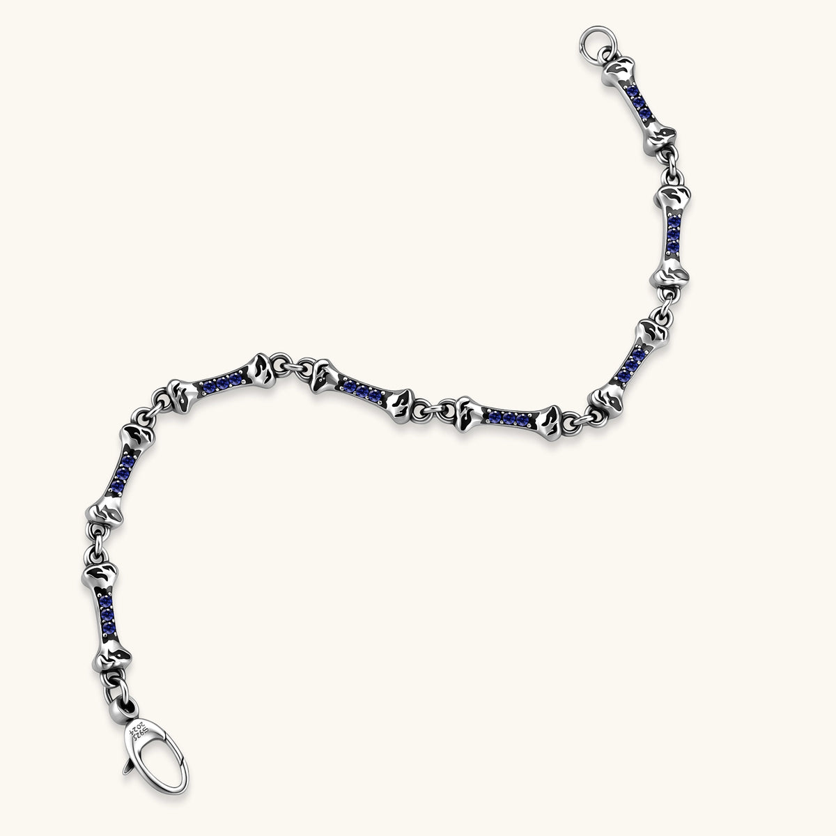 Sterling silver bone-link bracelet with blue cubic zirconia stones and engraved motifs, lobster clasp, on cream background.