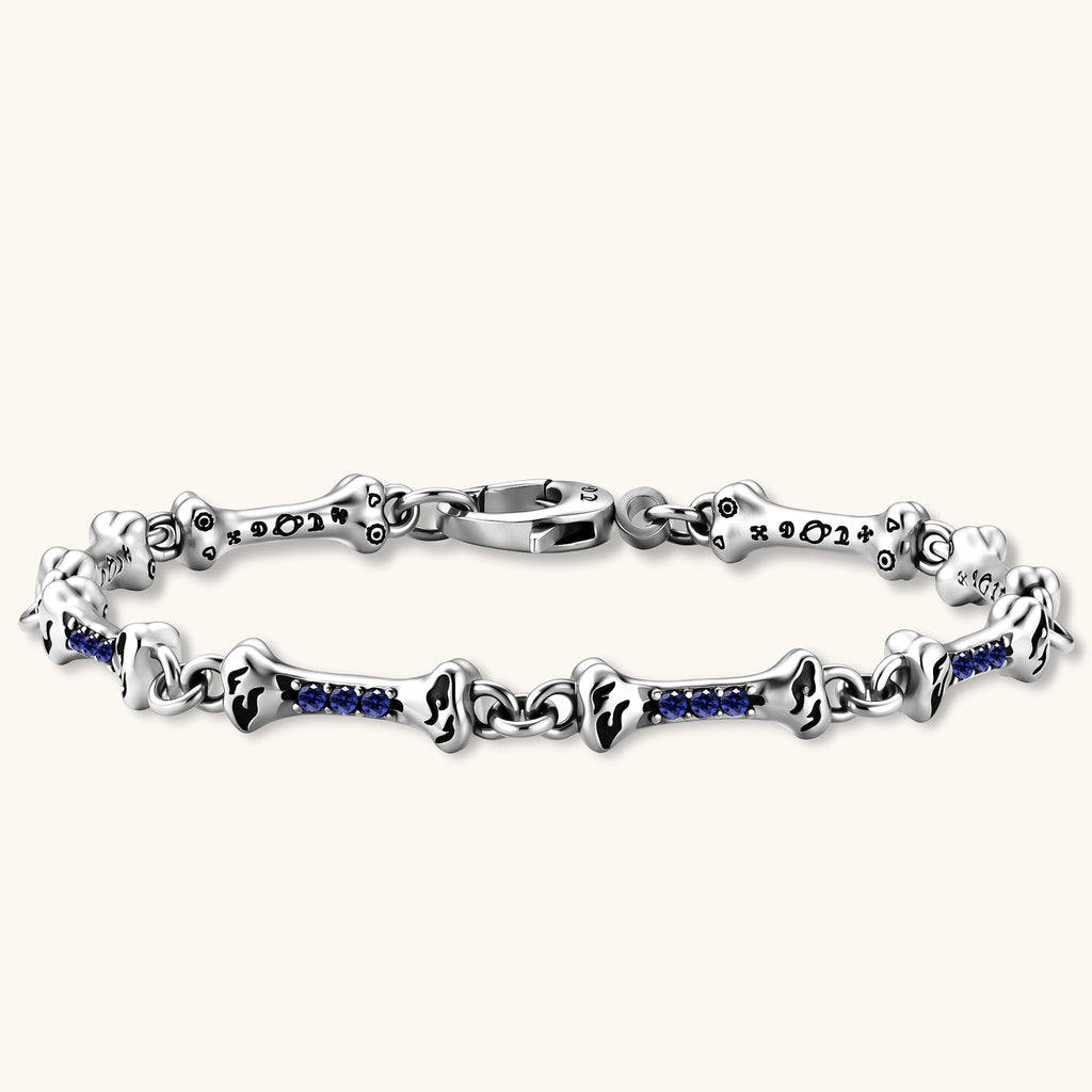 Sterling silver bone-link bracelet with blue cubic zirconia stones and engraved motifs, lobster clasp, on cream background.