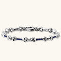 Sterling silver bone-link bracelet with blue cubic zirconia stones and engraved motifs, lobster clasp, on cream background.