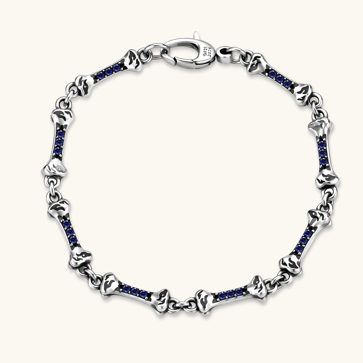 Sterling silver bone-link bracelet with blue cubic zirconia stones and engraved motifs, lobster clasp, on cream background.